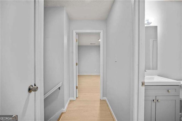 corridor with a sink, light wood-style flooring, baseboards, and a textured ceiling