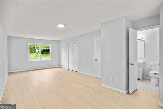 unfurnished bedroom with ensuite bathroom, light wood-style floors, baseboards, and a closet