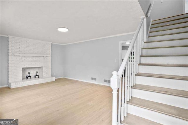 unfurnished living room with wood finished floors, visible vents, baseboards, stairs, and crown molding