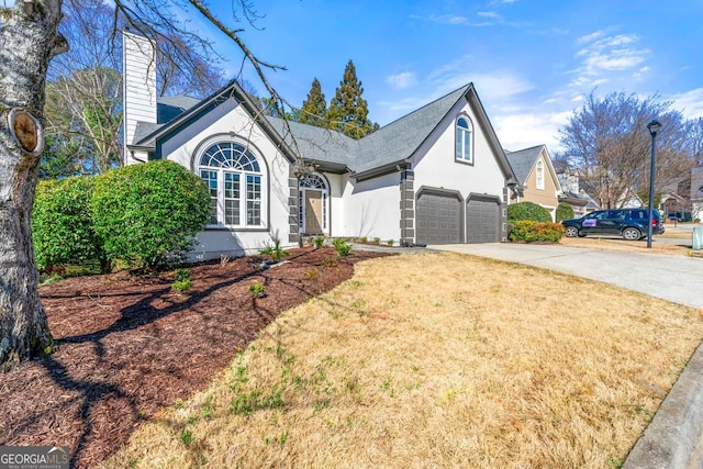 view of front of property with a front yard, driveway, an attached garage, a chimney, and stucco siding