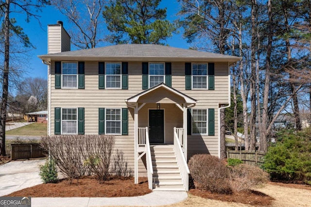 colonial home featuring a chimney and fence