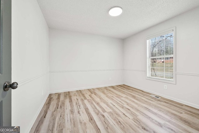 spare room with visible vents, a textured ceiling, baseboards, and wood finished floors