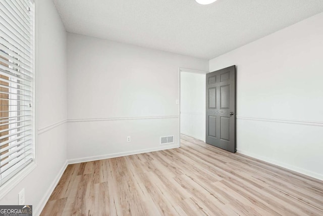 unfurnished bedroom featuring a textured ceiling, light wood-style floors, visible vents, and baseboards