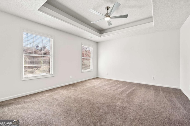 empty room with baseboards, carpet floors, a textured ceiling, a raised ceiling, and a ceiling fan