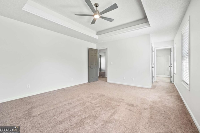 unfurnished bedroom with baseboards, ensuite bath, a textured ceiling, a raised ceiling, and light colored carpet