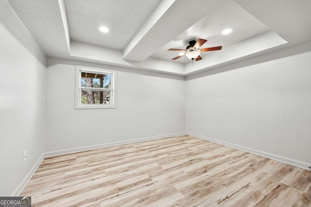 unfurnished room with a tray ceiling, baseboards, wood finished floors, and a ceiling fan