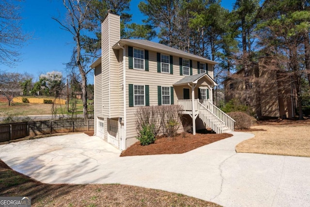 colonial-style house with driveway, fence, stairway, an attached garage, and a chimney