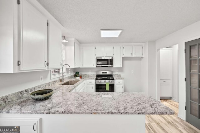 kitchen featuring light stone counters, white cabinets, appliances with stainless steel finishes, and a sink