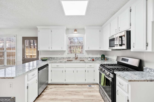 kitchen with light stone counters, appliances with stainless steel finishes, a peninsula, white cabinetry, and a sink