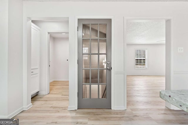 hall with light wood-style flooring, a textured ceiling, and baseboards