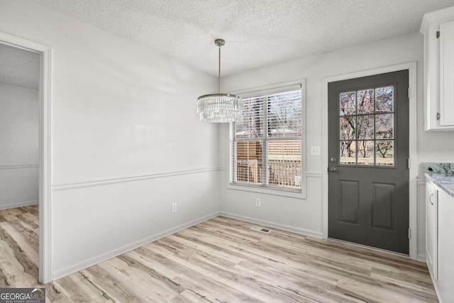 unfurnished dining area with baseboards, visible vents, an inviting chandelier, a textured ceiling, and light wood-type flooring