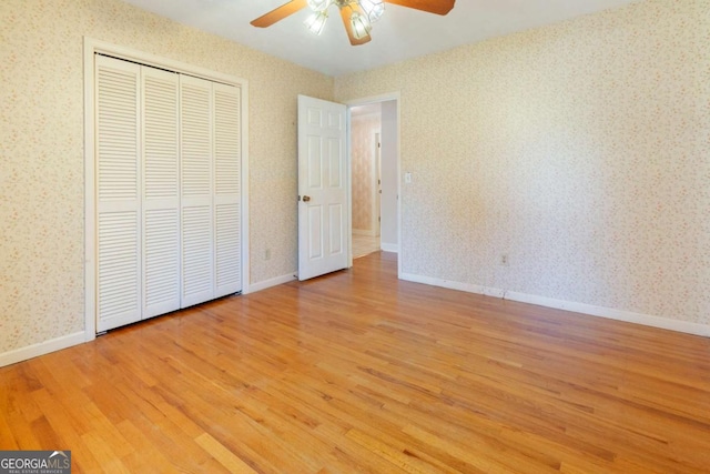 unfurnished bedroom featuring a ceiling fan, baseboards, wallpapered walls, light wood-style floors, and a closet