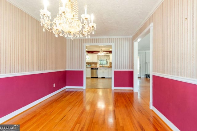 unfurnished dining area featuring a notable chandelier, crown molding, and wallpapered walls