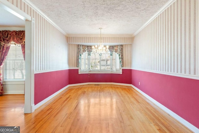 unfurnished dining area featuring a chandelier, crown molding, baseboards, and wood finished floors