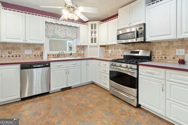 kitchen featuring a ceiling fan, a sink, appliances with stainless steel finishes, white cabinets, and decorative backsplash