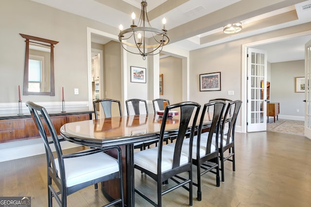 dining area with a chandelier, a raised ceiling, visible vents, and wood finished floors