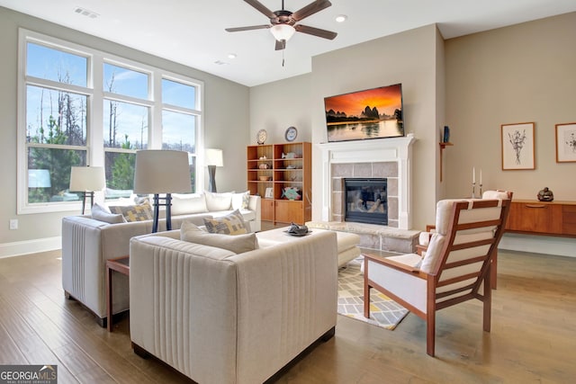 living room featuring visible vents, baseboards, a tile fireplace, wood finished floors, and a ceiling fan