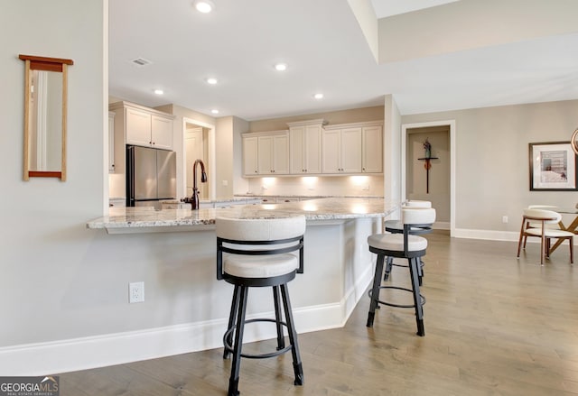 kitchen featuring light wood finished floors, light stone countertops, a kitchen bar, a peninsula, and freestanding refrigerator