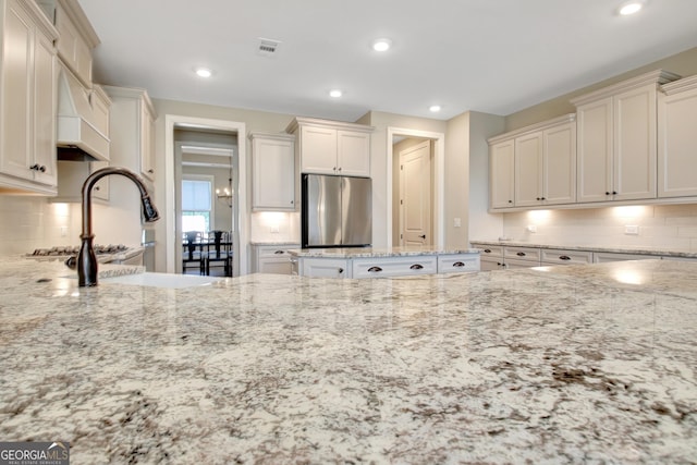 kitchen with light stone counters, visible vents, freestanding refrigerator, and a sink