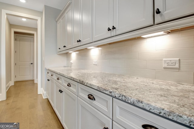 kitchen featuring light stone counters, light wood-style floors, backsplash, and white cabinets