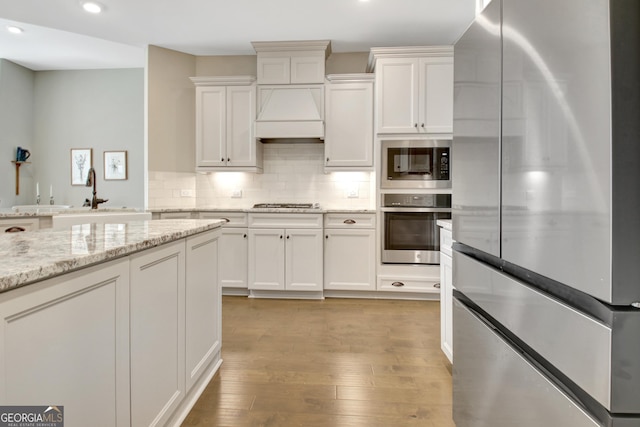 kitchen with premium range hood, stainless steel appliances, decorative backsplash, white cabinets, and light wood-type flooring