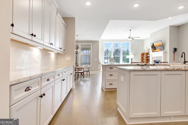 kitchen featuring light wood finished floors, decorative backsplash, a fireplace, white cabinetry, and a ceiling fan