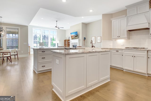 kitchen featuring light wood-type flooring, a kitchen island, white cabinets, ceiling fan with notable chandelier, and tasteful backsplash