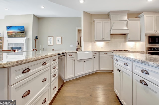 kitchen with a peninsula, custom range hood, light wood-style floors, appliances with stainless steel finishes, and backsplash