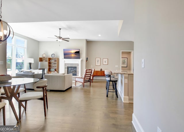 dining area with baseboards, ceiling fan, a tiled fireplace, recessed lighting, and wood finished floors