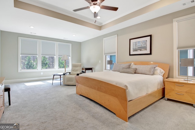 bedroom with light carpet, visible vents, a tray ceiling, and baseboards