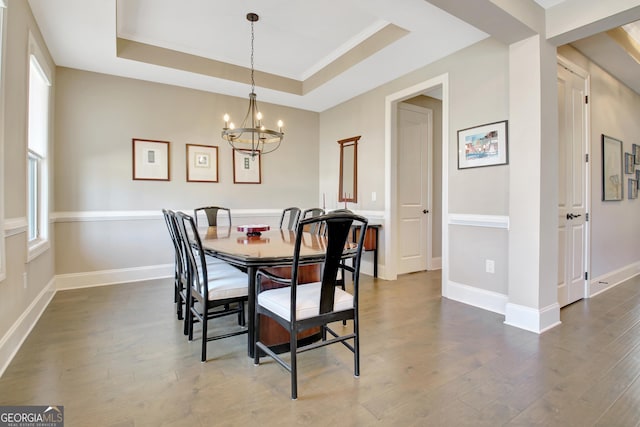 dining space featuring dark wood-style floors, a chandelier, a raised ceiling, and baseboards