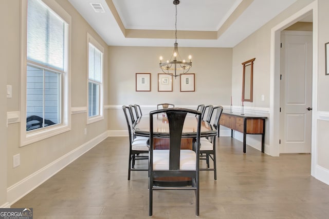 dining area featuring visible vents, a raised ceiling, an inviting chandelier, and wood finished floors