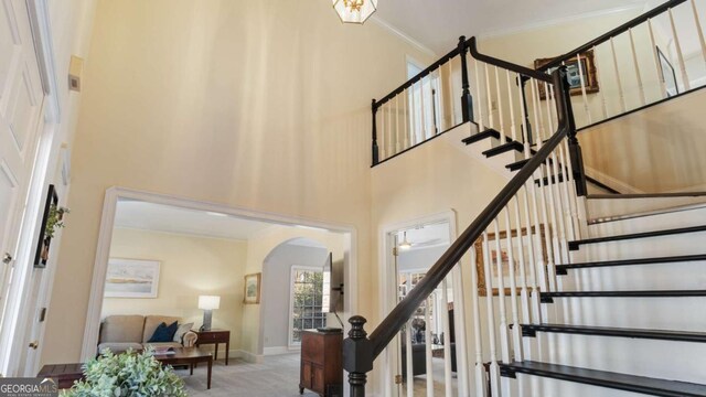 stairway featuring ornamental molding, carpet, baseboards, a high ceiling, and arched walkways