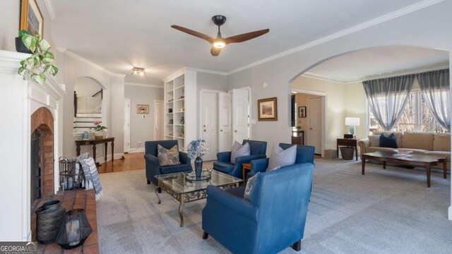 carpeted living area featuring arched walkways, ornamental molding, a fireplace, and a ceiling fan