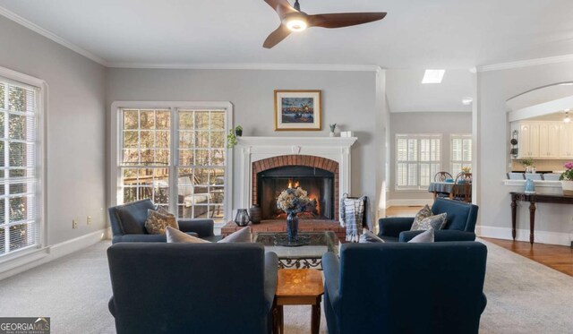 living room with baseboards, a fireplace, ornamental molding, and a ceiling fan