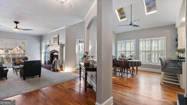 living room featuring a brick fireplace, wood finished floors, a ceiling fan, and ornamental molding