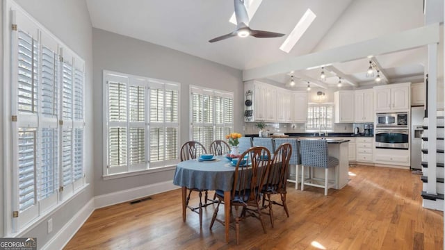 dining space with visible vents, baseboards, ceiling fan, vaulted ceiling with skylight, and light wood-style floors