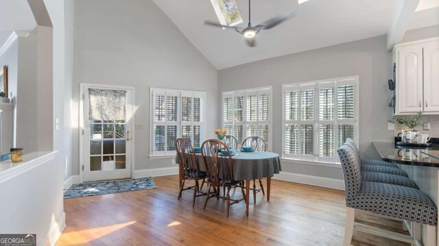 dining room featuring high vaulted ceiling, a skylight, baseboards, a ceiling fan, and light wood-type flooring