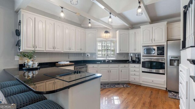 kitchen featuring a peninsula, dark countertops, appliances with stainless steel finishes, a sink, and a kitchen breakfast bar