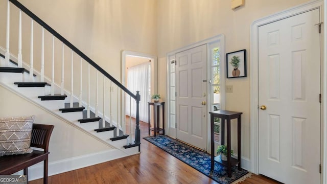 entrance foyer featuring a towering ceiling, stairs, baseboards, and wood finished floors