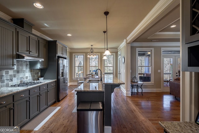 kitchen featuring a sink, appliances with stainless steel finishes, under cabinet range hood, a notable chandelier, and tasteful backsplash