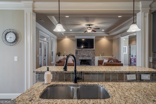 kitchen featuring a tray ceiling, decorative columns, a fireplace, and a sink