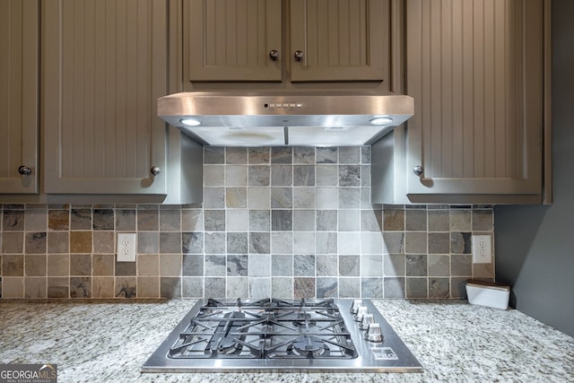 kitchen featuring stainless steel gas cooktop, decorative backsplash, light stone counters, and under cabinet range hood