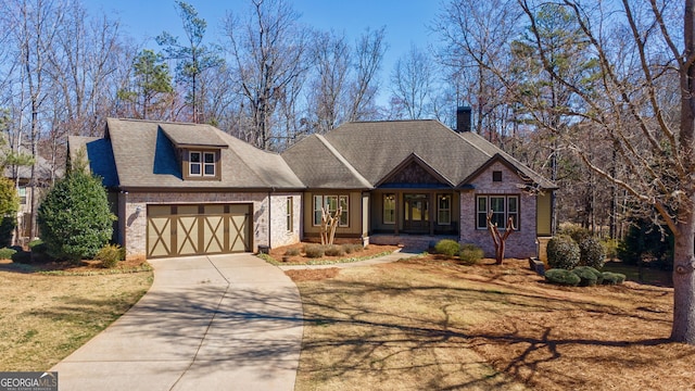 craftsman house with a front yard, driveway, an attached garage, a shingled roof, and brick siding