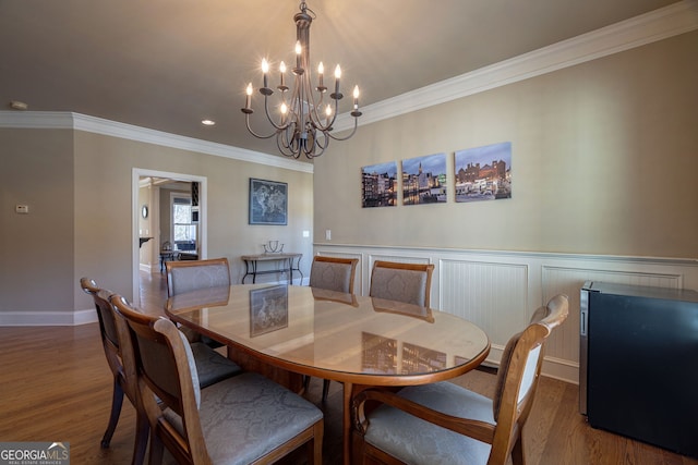 dining room with wood finished floors, baseboards, ornamental molding, wainscoting, and a notable chandelier