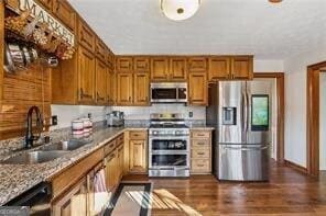 kitchen featuring brown cabinetry, baseboards, dark wood finished floors, a sink, and appliances with stainless steel finishes