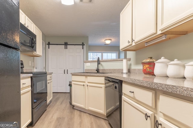 kitchen featuring light wood-type flooring, black appliances, a sink, a textured ceiling, and a peninsula