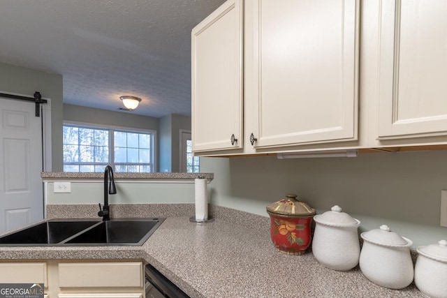 kitchen with white cabinets, a textured ceiling, light countertops, and a sink