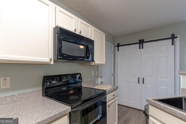 kitchen with white cabinetry, black appliances, a barn door, and light countertops