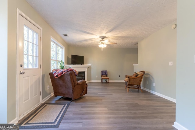 interior space with visible vents, a textured ceiling, a glass covered fireplace, wood finished floors, and ceiling fan